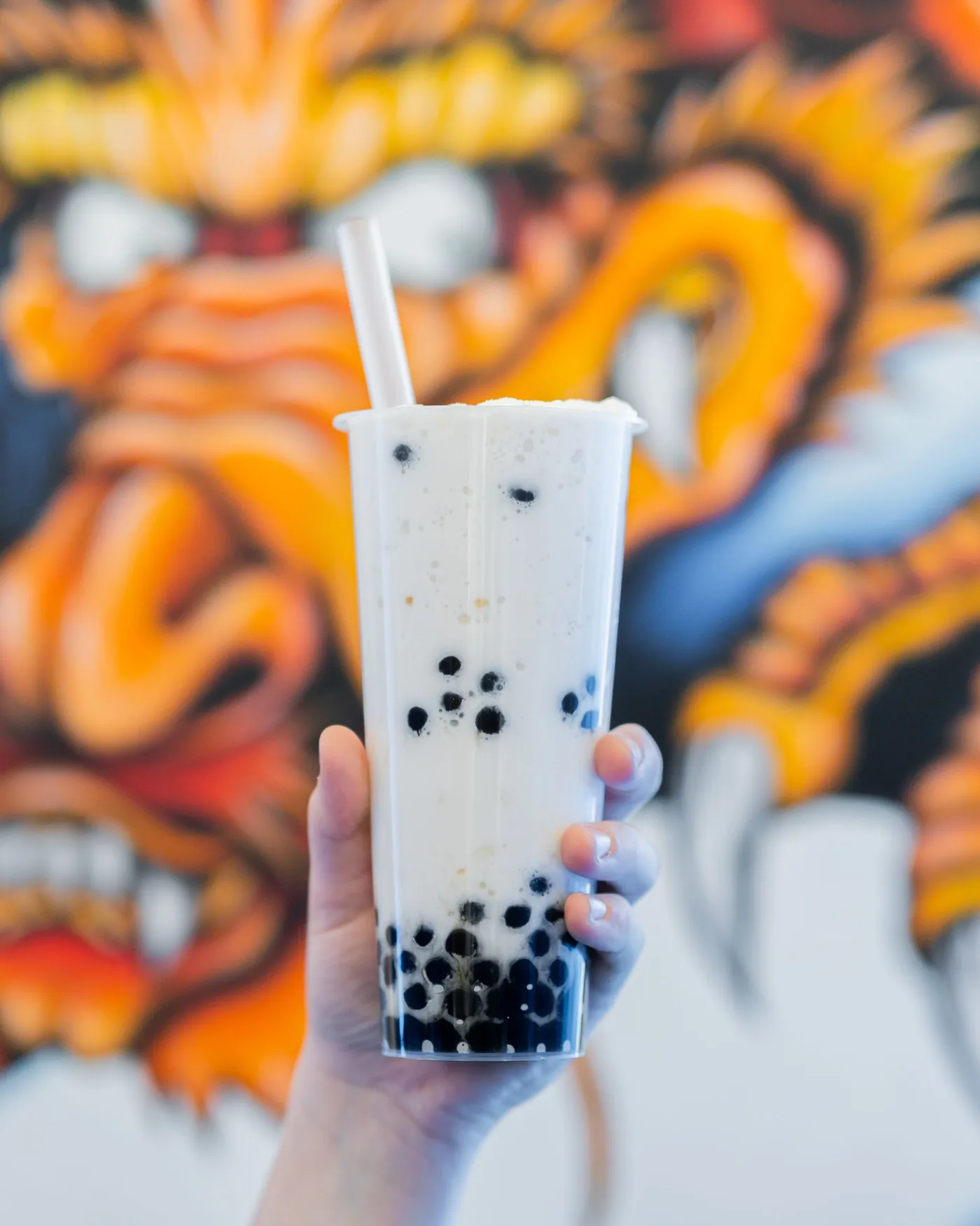 A hand holding a bubble tea with tapioca pearls in front of a painted dragon mural