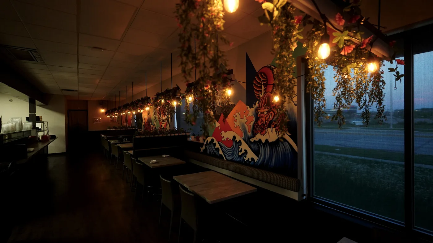 A long view down the dining room's booths under string lights and hanging plants