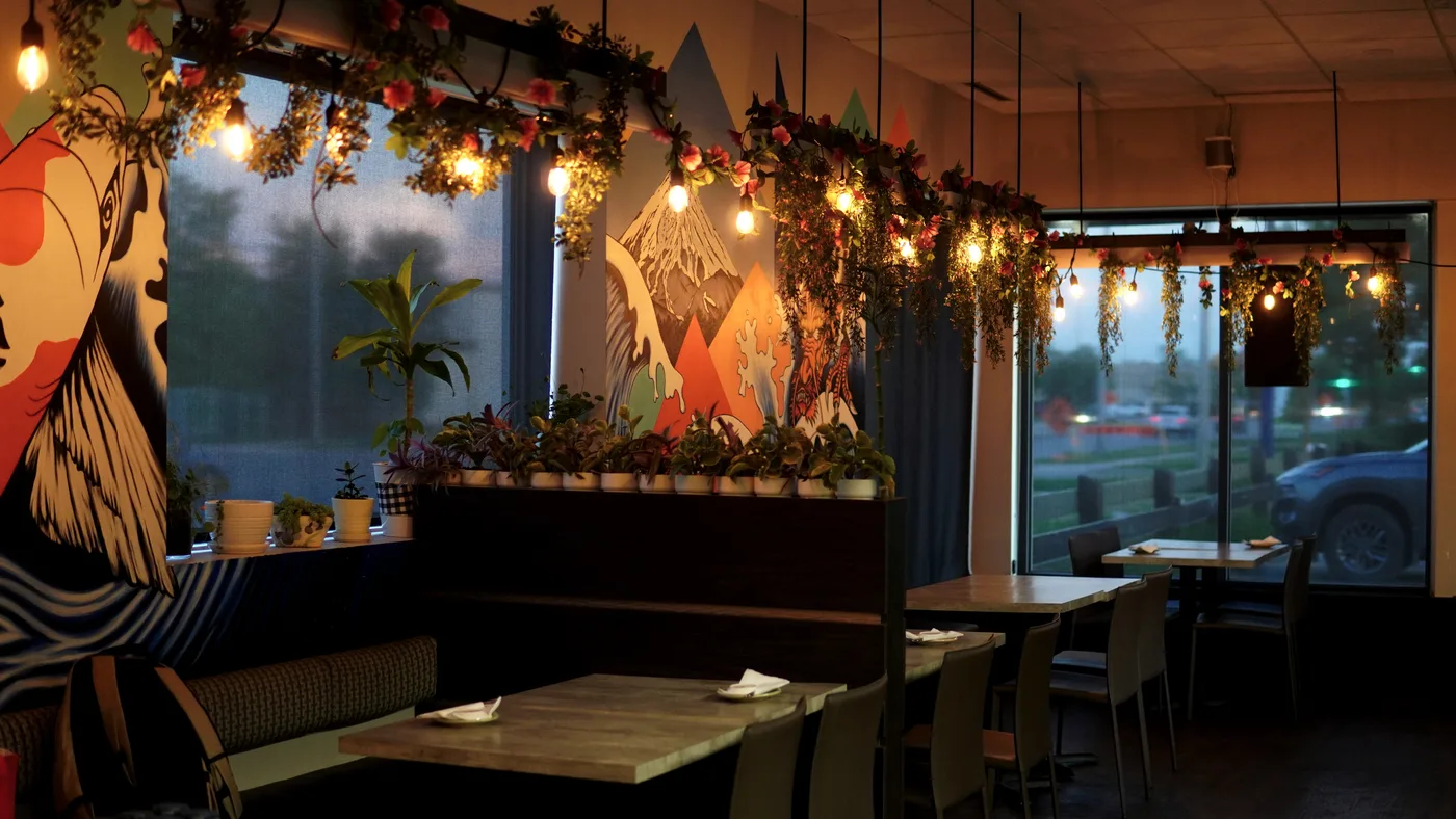 The dining room at dusk: a painted wave mural, string lights and hanging plants above the tables