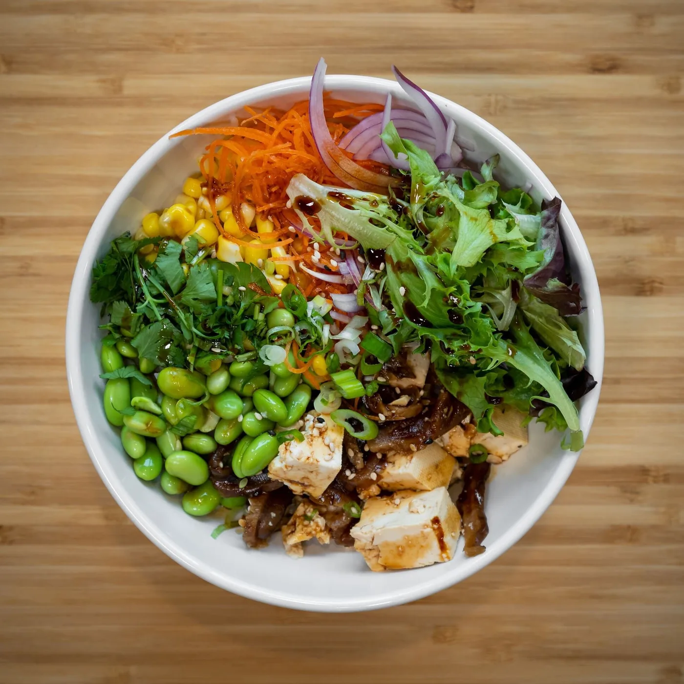 A build-your-own poke bowl with tofu, edamame, corn, carrots, mixed greens and red onion