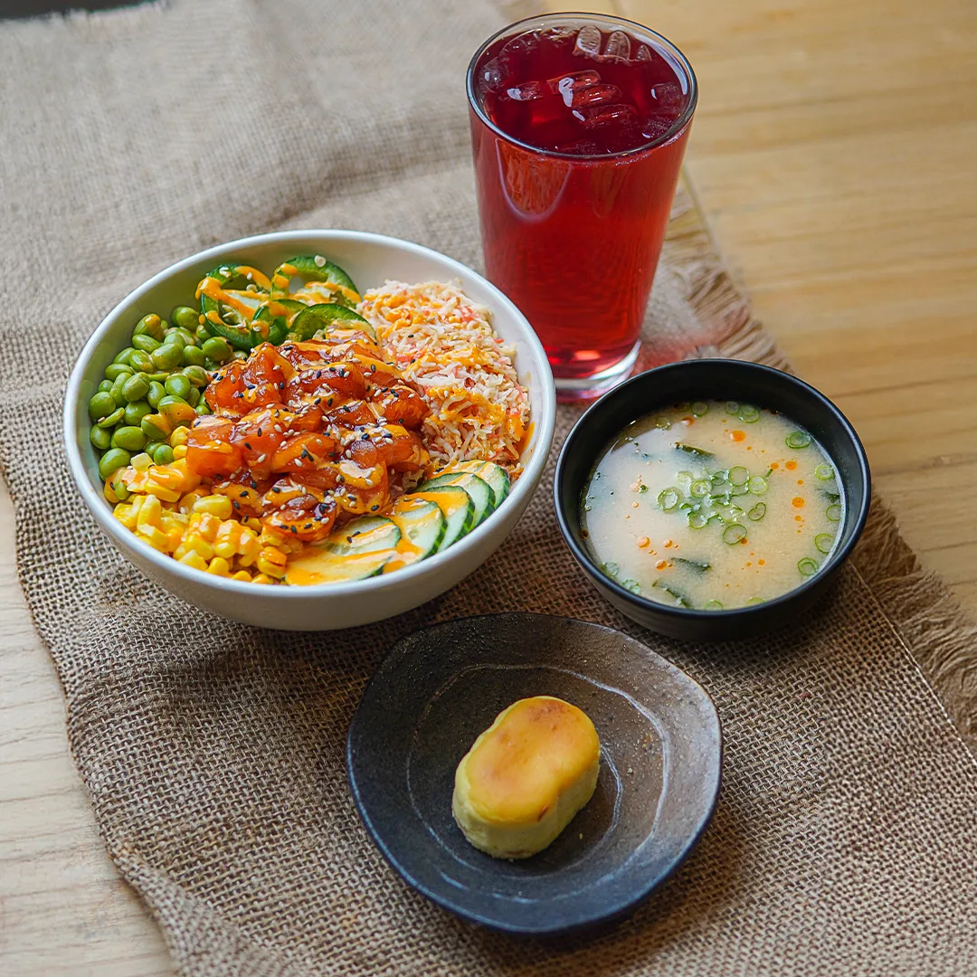A poke bowl with a red iced drink, a cup of miso soup and a small Japanese cheesecake
