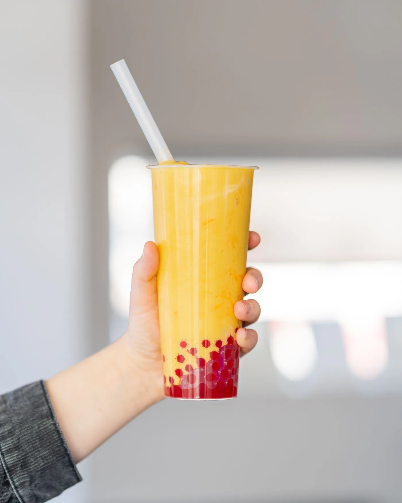 A hand holding a mango bubble tea with red pearls