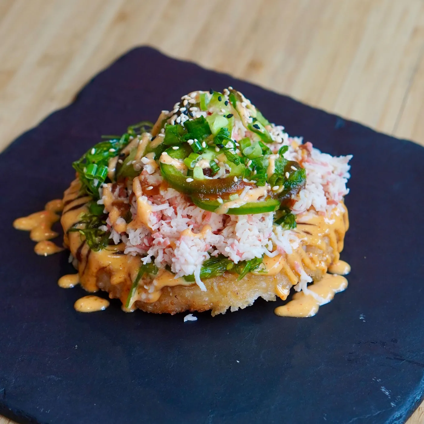 A California sushi pizza topped with crab, seaweed salad, jalapeño and spicy mayo on a slate