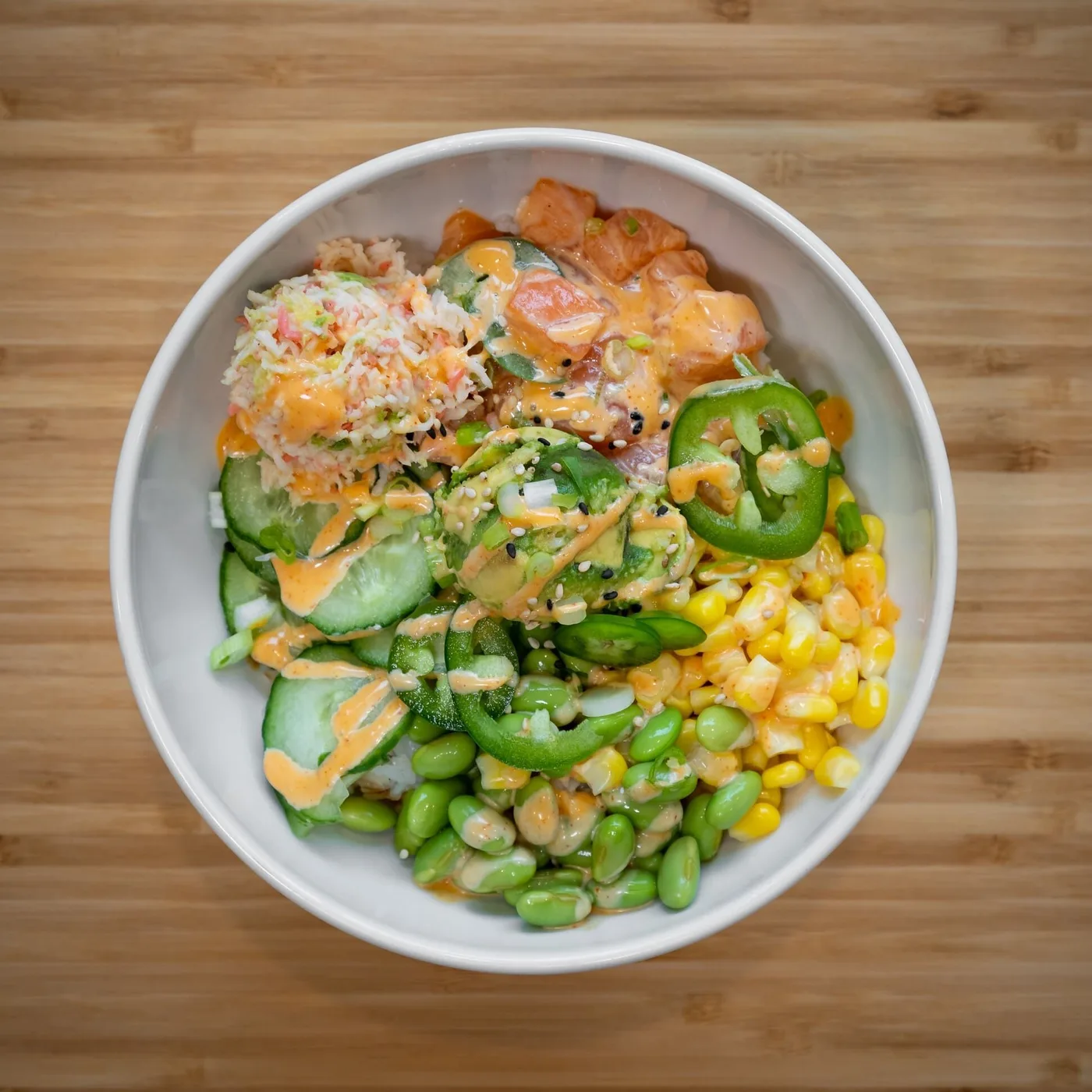 A salmon poke bowl topped with crab meat, edamame, cucumber, corn, jalapeño slices and spicy mayo